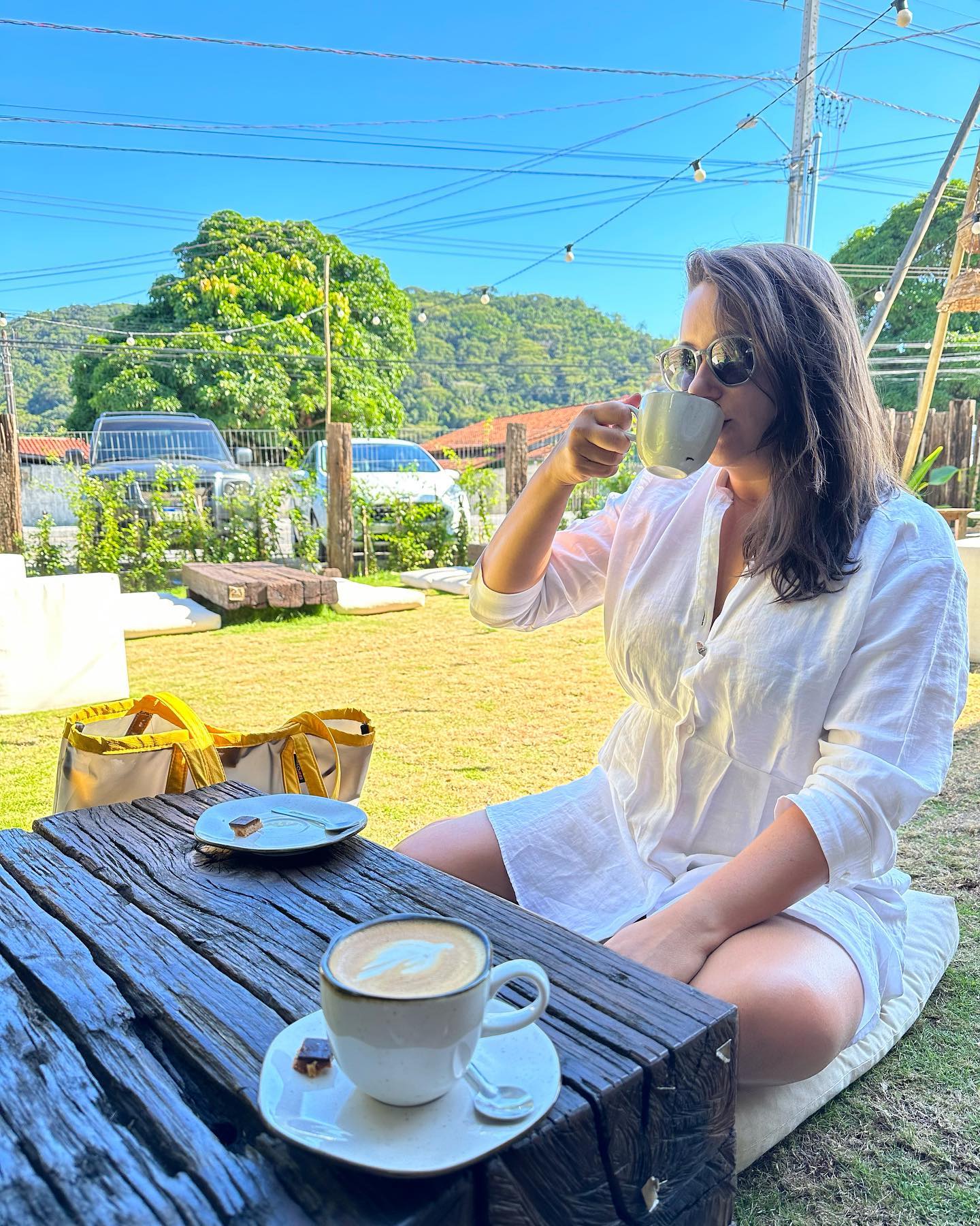 Nay Fiorini sentada no chão tomando café ao ar livre
